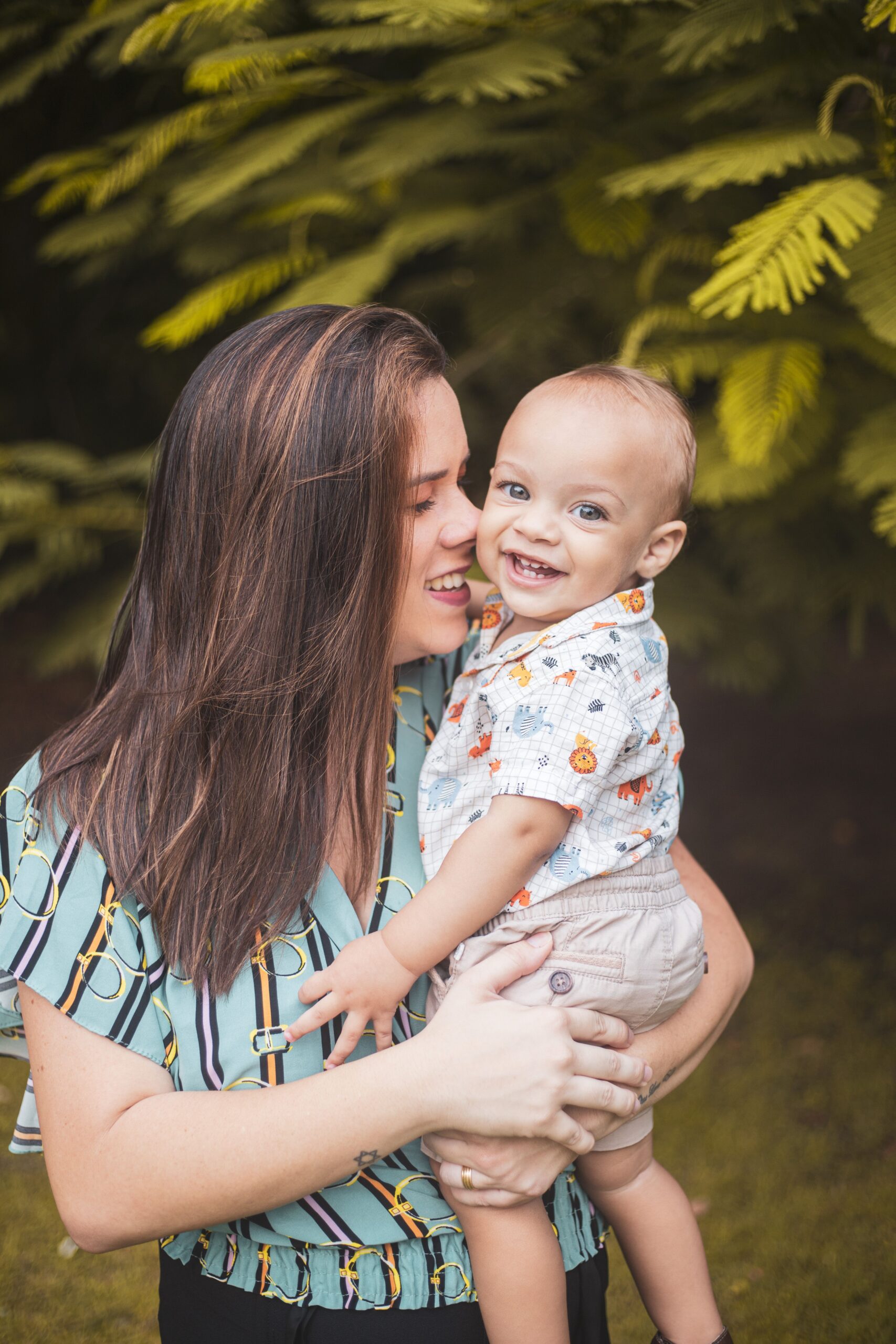 A heartwarming moment between a smiling mother and her baby outdoors with lush greenery.